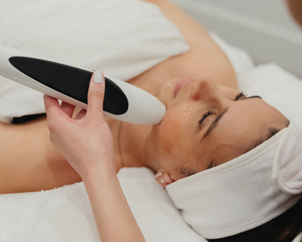 Woman receiving a facial treatment with a device held by a professional.